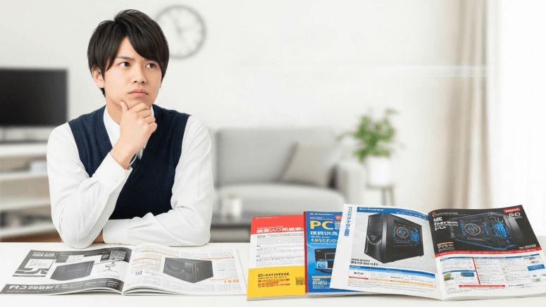 カタログやスマホを見ながら真剣にゲーミングPCを選んでいる大学生